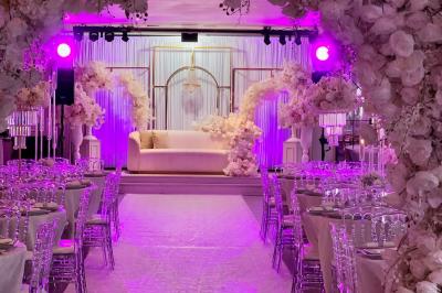 Salle de réception élégante avec tables décorées de fleurs blanches, chaises transparentes et éclairage tamisé.