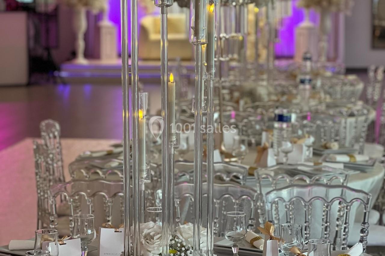 Table de réception élégamment décorée avec chandeliers, fleurs blanches et détails dorés dans une salle lumineuse.