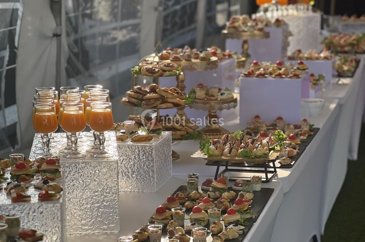 Buffet élégant avec verrines, amuse-bouches variés et boissons disposés sur une longue table blanche en extérieur.