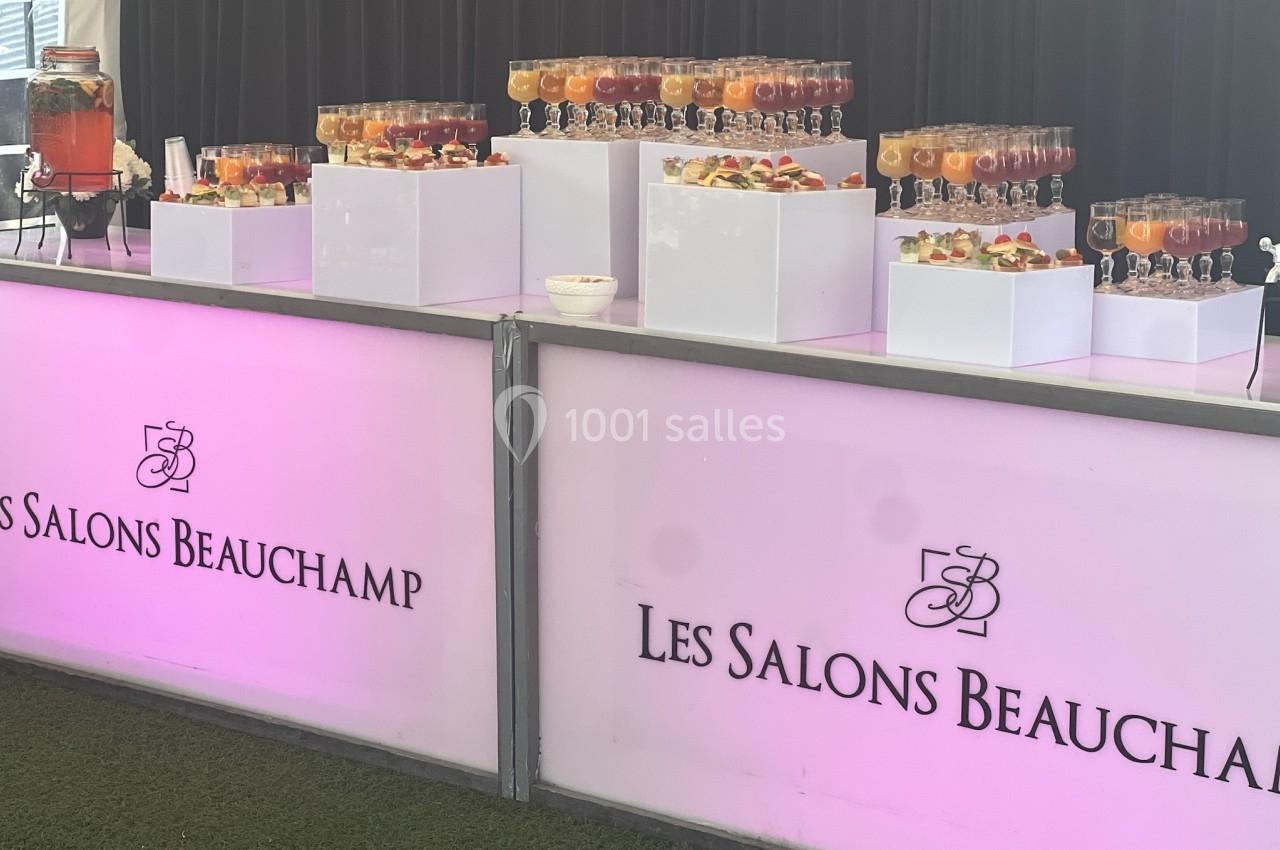 Buffet de boissons colorées disposées sur des présentoirs blancs, avec un panneau lumineux ’Les Salons Beauchamp’.