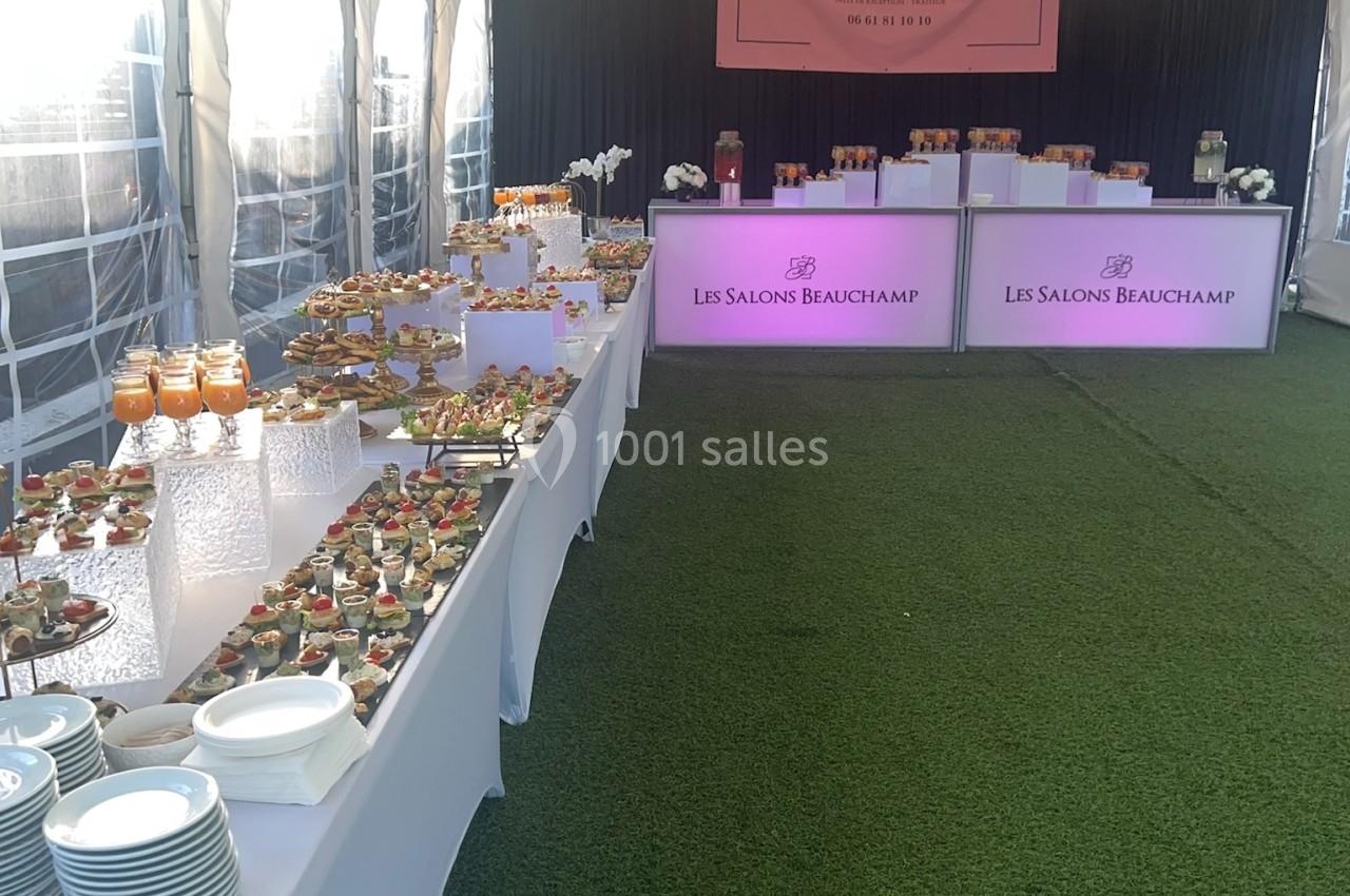 Buffet de réception sous une tente avec tables garnies de plats variés et décoration élégante sur gazon synthétique.