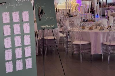 Salle de réception élégante avec tables décorées de fleurs blanches, chaises transparentes et éclairage tamisé.