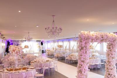 Salle de réception élégante avec tables décorées de fleurs blanches, chaises transparentes et éclairage tamisé.