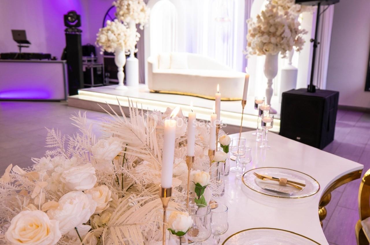 Table décorée avec des bougies, fleurs blanches et vaisselle élégante, dans une salle de réception lumineuse.