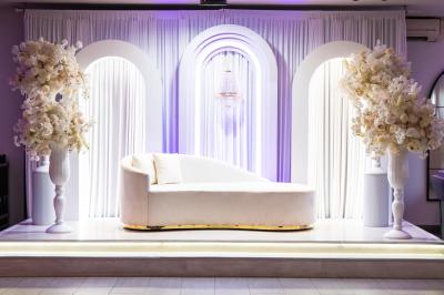Salle de réception élégante avec tables décorées de fleurs blanches, chaises transparentes et éclairage tamisé.