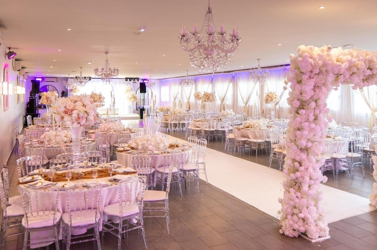 Salle de réception élégante décorée de fleurs blanches, avec tables dressées et chaises transparentes.