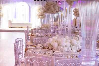 Salle de réception élégante avec tables décorées de fleurs blanches, chaises transparentes et éclairage tamisé.