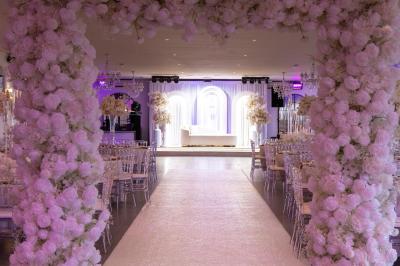 Salle de réception élégante avec tables décorées de fleurs blanches, chaises transparentes et éclairage tamisé.