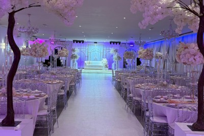 Salle de réception décorée pour un mariage, avec des tables élégantes, des fleurs blanches et une arche florale au premier…