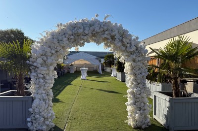 Salle de réception décorée pour un mariage, avec des tables élégantes, des fleurs blanches et une arche florale au premier…