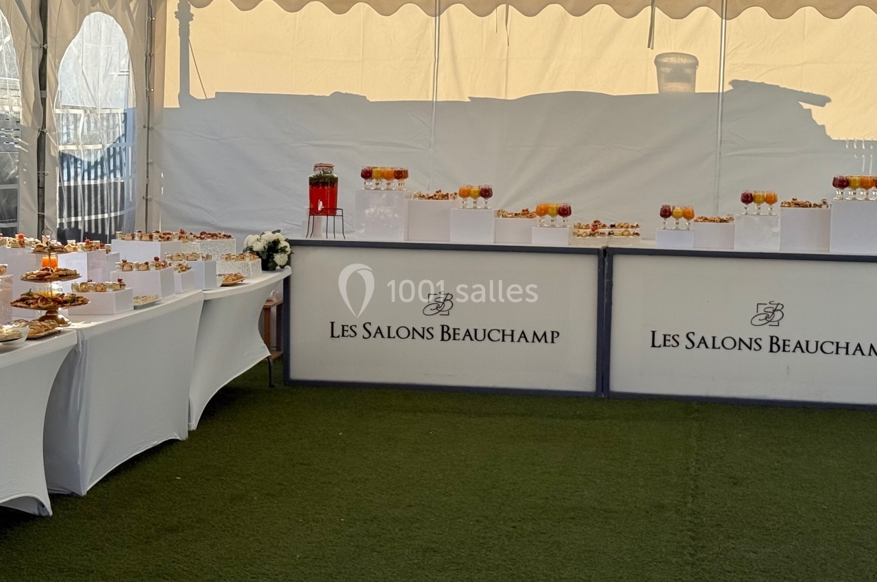 Buffet dressé sous une tente avec des boissons et des amuse-bouches sur des tables blanches.