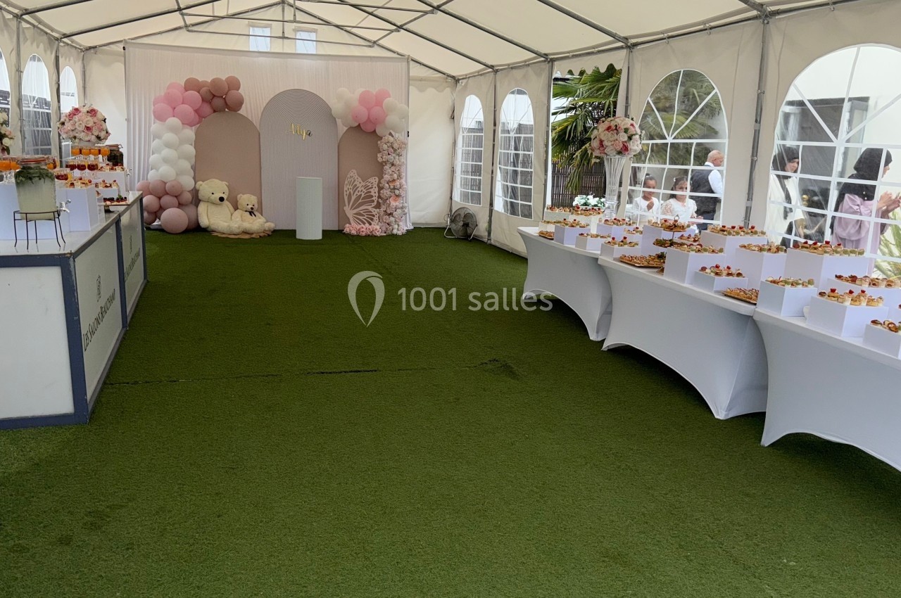 Intérieur d'une tente décorée pour un événement, avec tables de buffet, ballons et arrangements floraux.