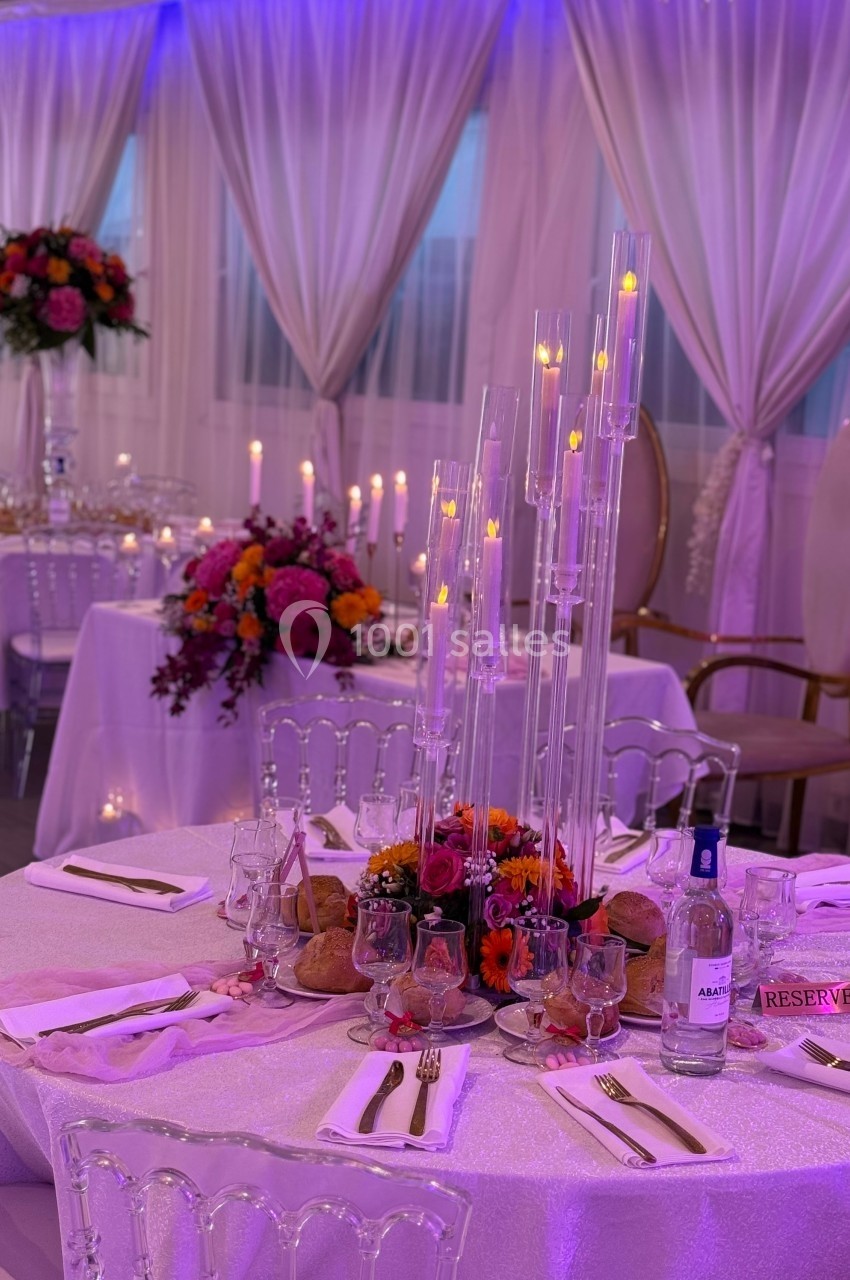 Salle de réception décorée avec des tables élégantes, bougies, fleurs colorées et nappes blanches.