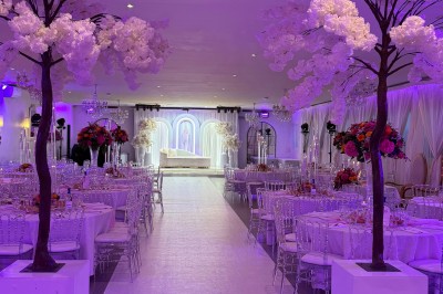 Salle de réception décorée pour un mariage, avec des tables élégantes, des fleurs blanches et une arche florale au premier…