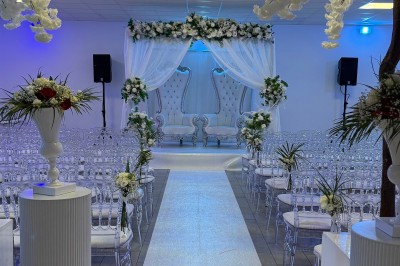 Salle de réception décorée pour un mariage, avec des tables élégantes, des fleurs blanches et une arche florale au premier…