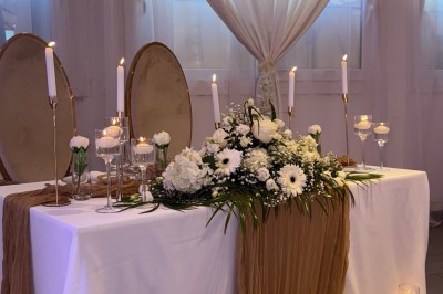 Salle de réception décorée pour un mariage, avec des tables élégantes, des fleurs blanches et une arche florale au premier…