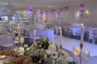 Salle de réception décorée pour un mariage, avec des tables élégantes, des fleurs blanches et une arche florale au premier…