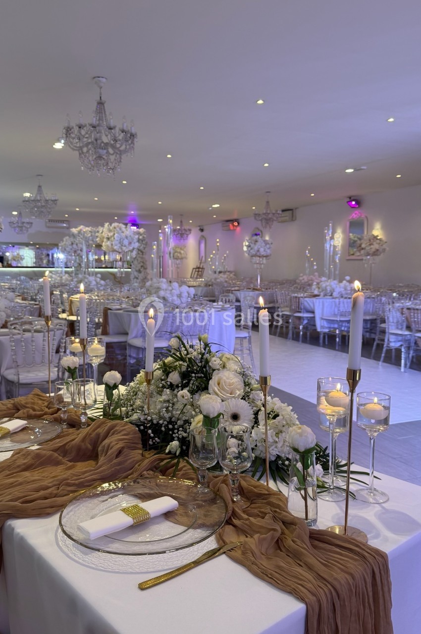 Salle de réception élégamment décorée avec chandeliers, bougies allumées et centre de table floral blanc.