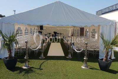 Salle de réception élégante avec tables décorées de fleurs blanches, chaises transparentes et éclairage tamisé.