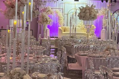 Salle de réception élégante avec tables décorées de fleurs blanches, chaises transparentes et éclairage tamisé.