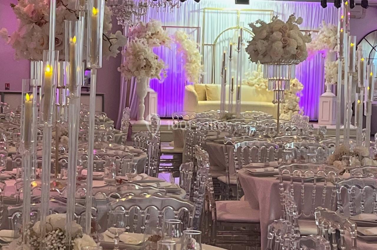 Salle de réception décorée avec des chandeliers, des fleurs blanches et des tables dressées pour un événement.