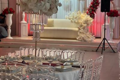 Salle de réception élégante avec tables décorées de fleurs blanches, chaises transparentes et éclairage tamisé.