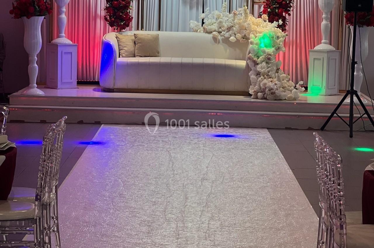 Canapé blanc décoré de fleurs blanches et rouges, placé sur une scène avec rideaux et éclairages colorés.