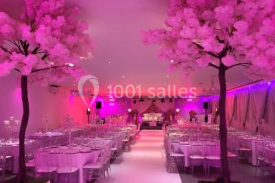 Salle de réception élégante avec tables décorées de fleurs blanches, chaises transparentes et éclairage tamisé.