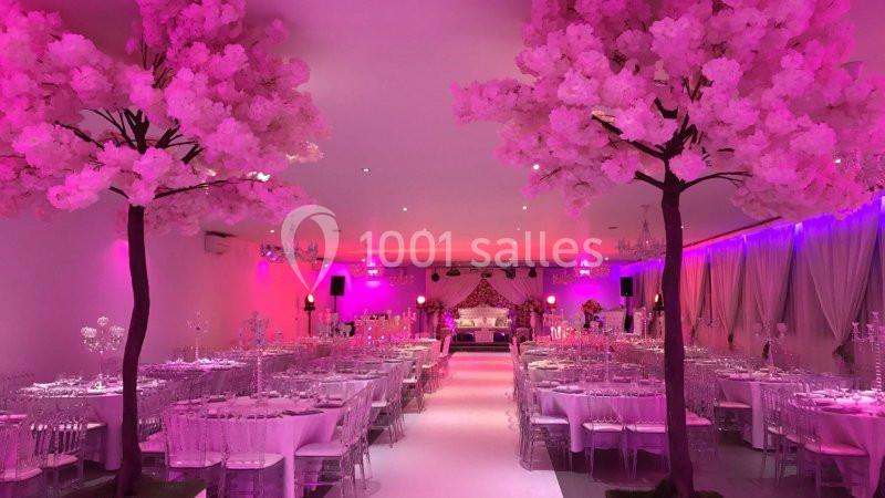 Salle de réception décorée avec des tables dressées, éclairage rose et arbres artificiels fleuris.