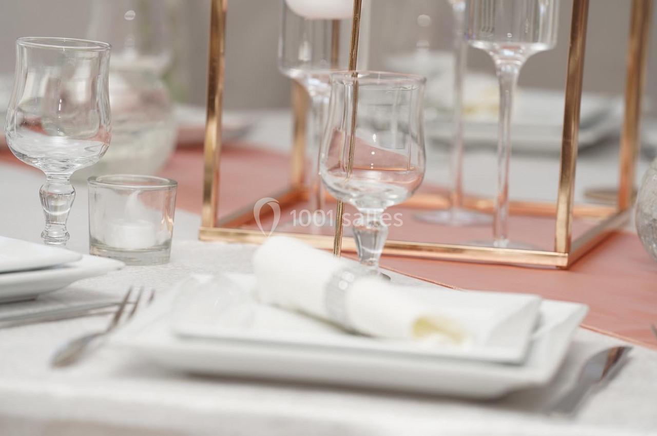 Table dressée avec des assiettes blanches, des verres, des couverts et une décoration en métal doré.