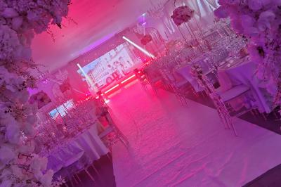 Salle de réception élégante avec tables décorées de fleurs blanches, chaises transparentes et éclairage tamisé.