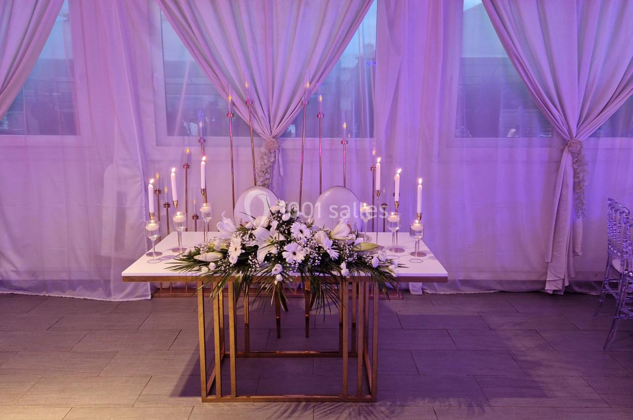 Table décorée pour un mariage avec des fleurs blanches, des bougies allumées et des rideaux violets en arrière-plan.