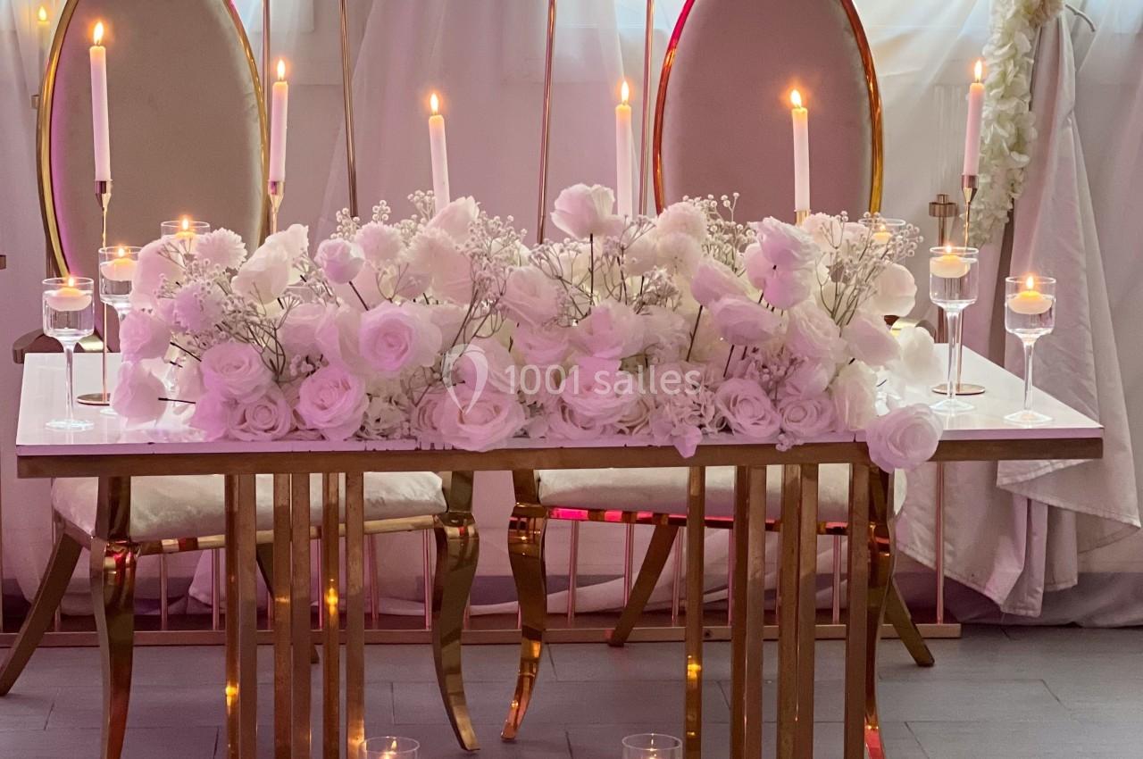 Table décorée avec des fleurs blanches et roses, entourée de bougies allumées et de chaises élégantes devant des rideaux.