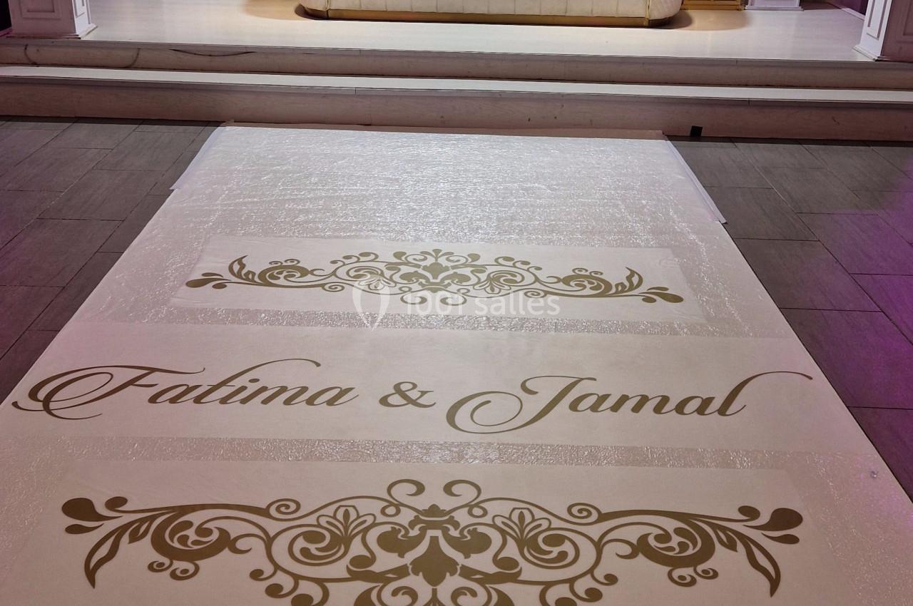 Allée décorative avec noms inscrits en doré menant à un canapé blanc devant une arche ornée de fleurs blanches.