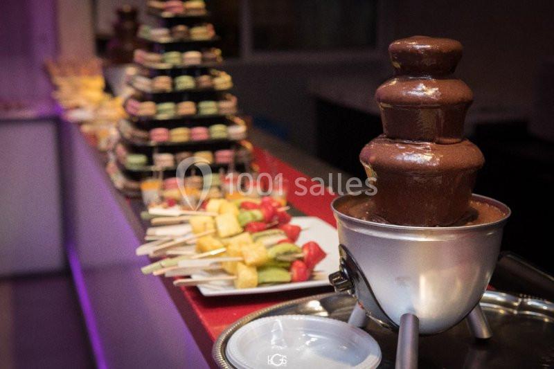 Fontaine de chocolat avec des brochettes de fruits et des macarons disposés sur une table de buffet.