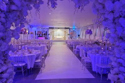 Salle de réception élégante avec tables décorées de fleurs blanches, chaises transparentes et éclairage tamisé.