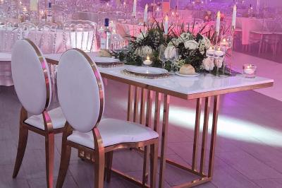 Salle de réception élégante avec tables décorées de fleurs blanches, chaises transparentes et éclairage tamisé.
