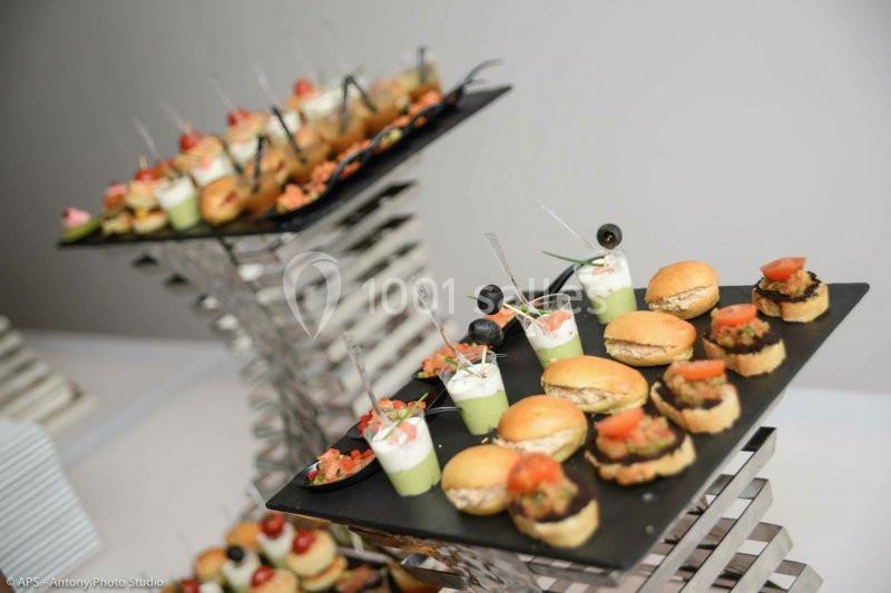 Plateaux de bouchées apéritives variées, incluant mini-burgers, verrines et amuse-bouches, présentés sur des supports…