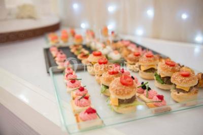 Salle de réception élégante avec tables décorées de fleurs blanches, chaises transparentes et éclairage tamisé.