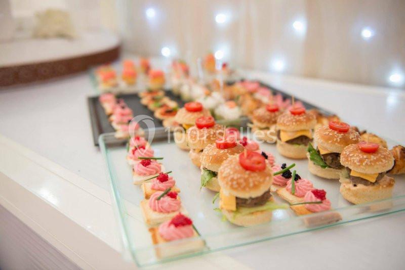 Plateau de mini-burgers et amuse-bouches variés disposés sur une table, éclairée par des lumières en arrière-plan.