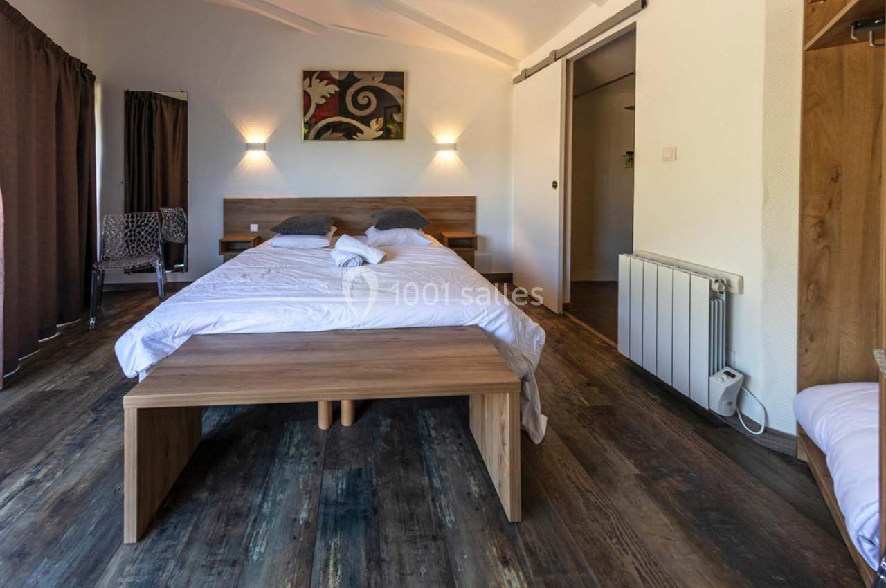 Chambre lumineuse avec lit double, parquet en bois, éclairage mural et rideaux sombres.