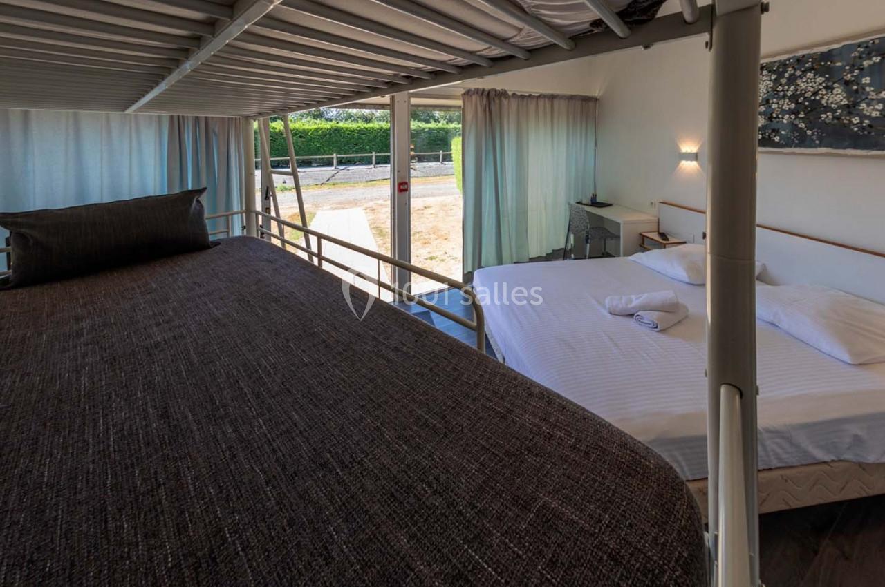 Lit superposé et lit double dans une chambre lumineuse avec vue sur l'extérieur, rideaux ouverts et décoration murale.