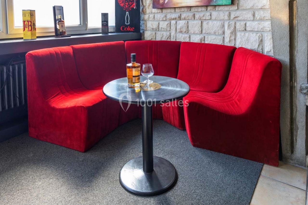 Banquette rouge en arc de cercle autour d'une table ronde avec une bouteille de whisky et un verre posé dessus.