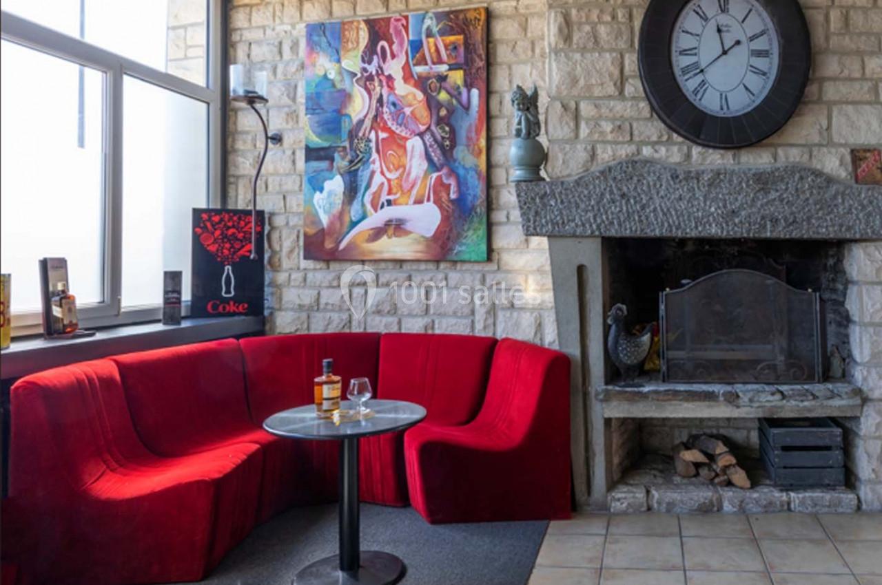 Canapé rouge en angle autour d'une table basse, cheminée en pierre et horloge murale dans un salon lumineux.