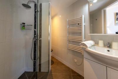 Salle de bain moderne avec douche à l'italienne, lavabo avec miroir, radiateur sèche-serviettes et carrelage clair.