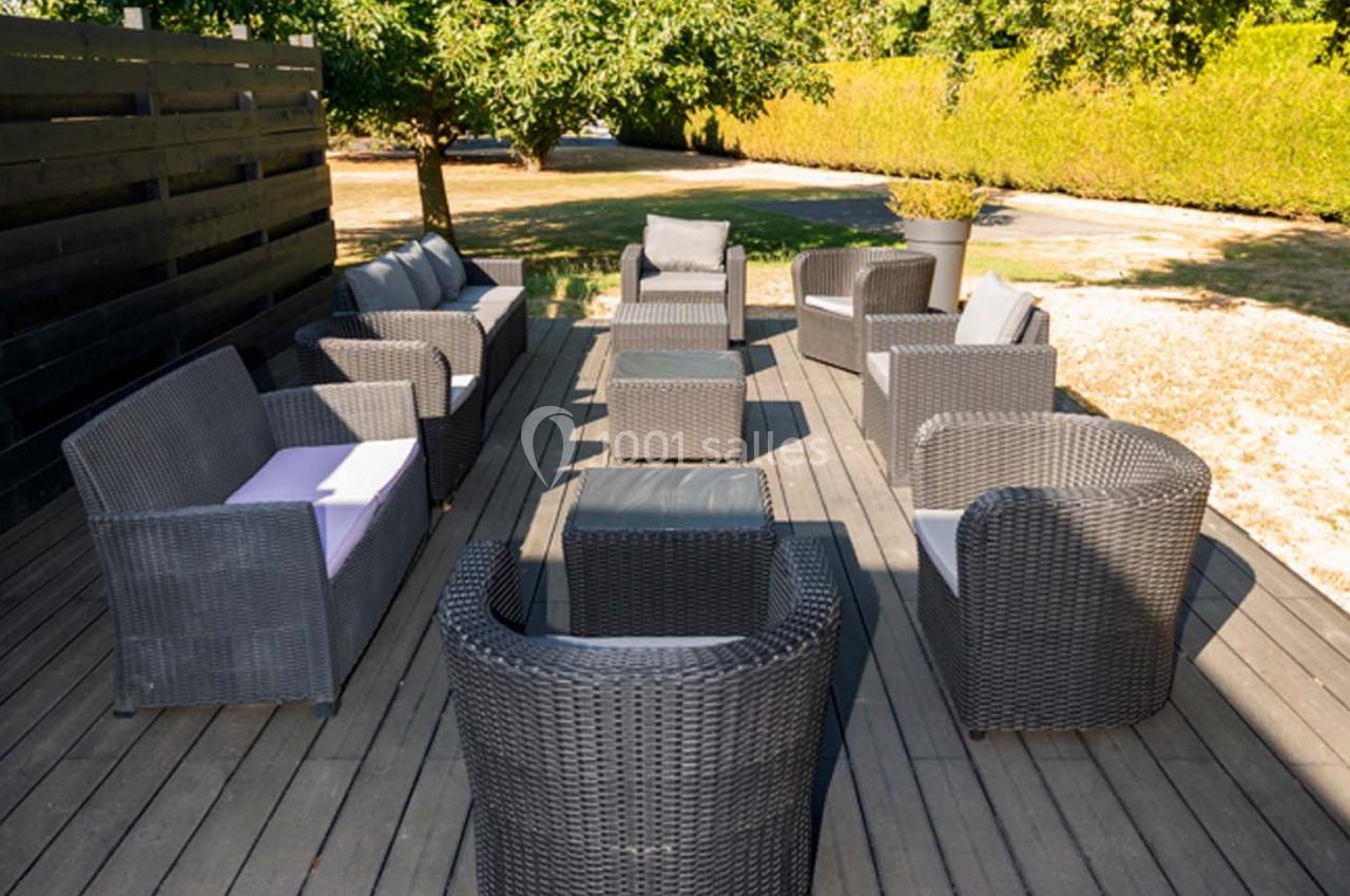 Salon de jardin en résine tressée avec fauteuils et canapés disposés en cercle sur une terrasse en bois, entourée de verdure.
