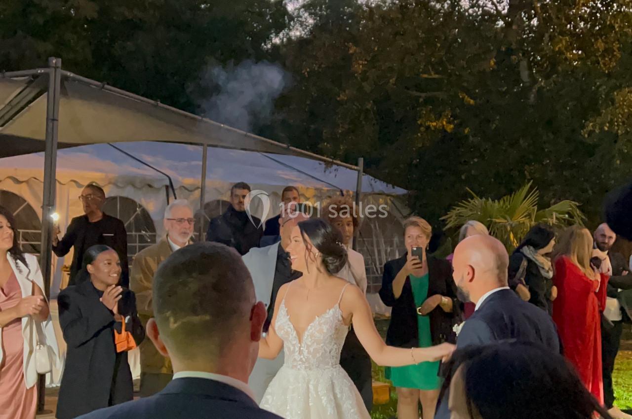 Un couple danse en extérieur lors d'une réception, entouré d'invités debout près d'une tente éclairée.