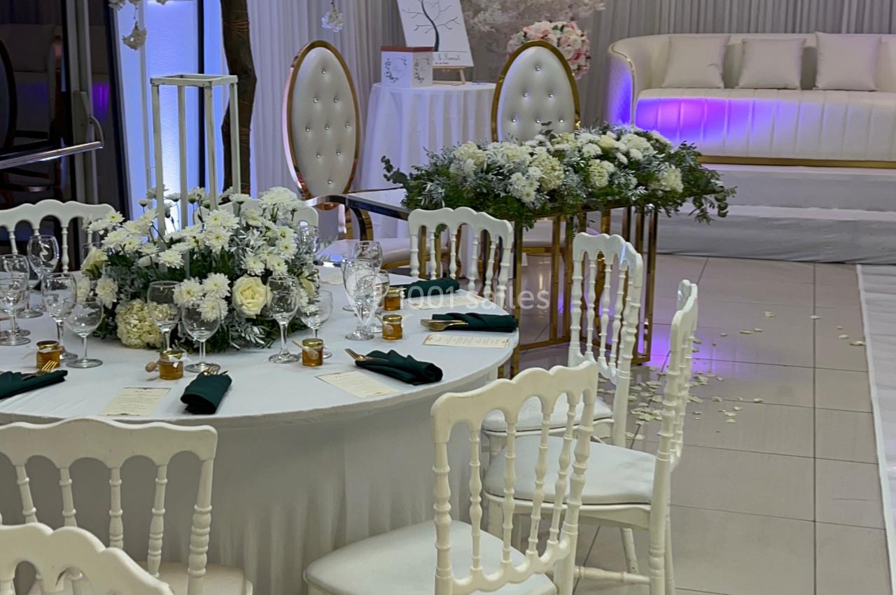 Salle de réception décorée avec des tables rondes, des chaises blanches, des fleurs et un espace avec canapé et éclairage…