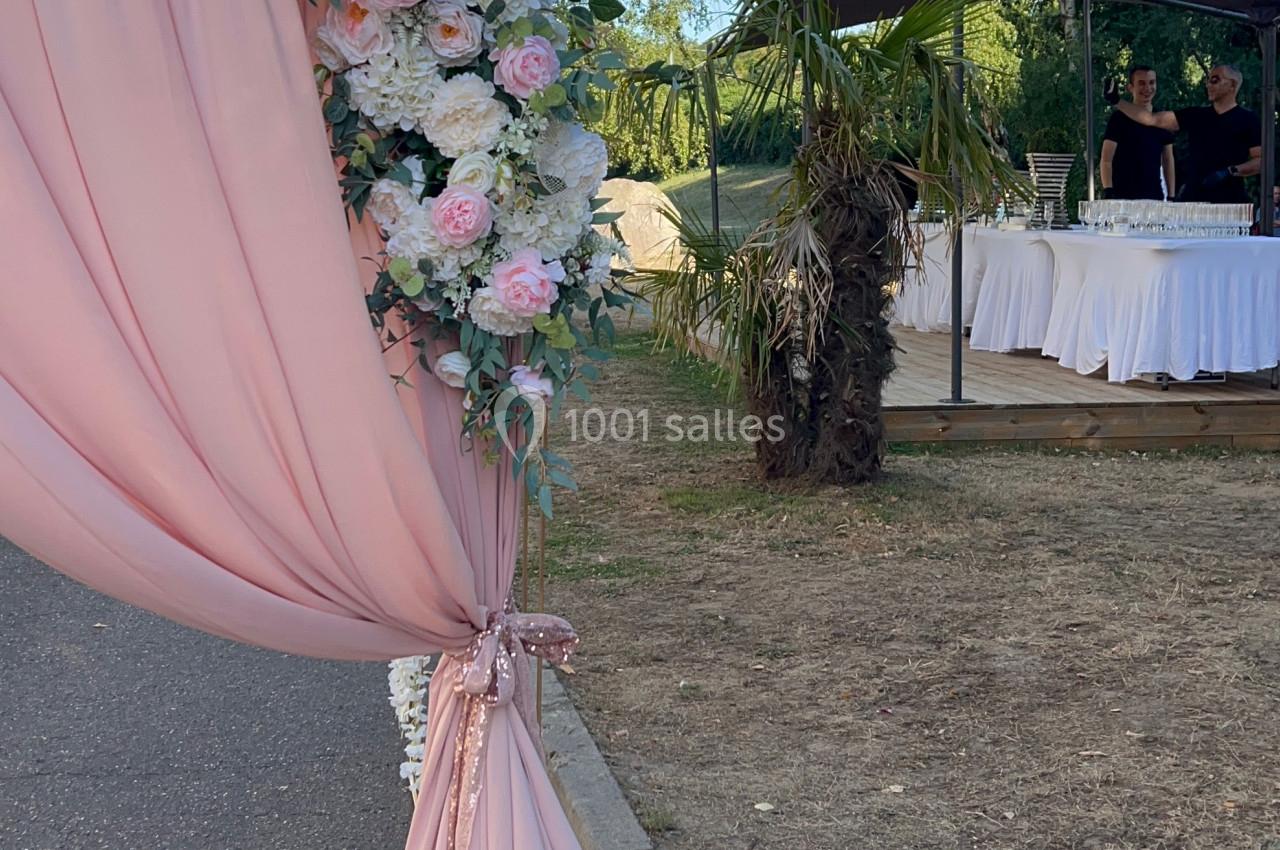 Rideau rose décoré de fleurs blanches et roses, installé en extérieur près d'une allée et d'une tente.