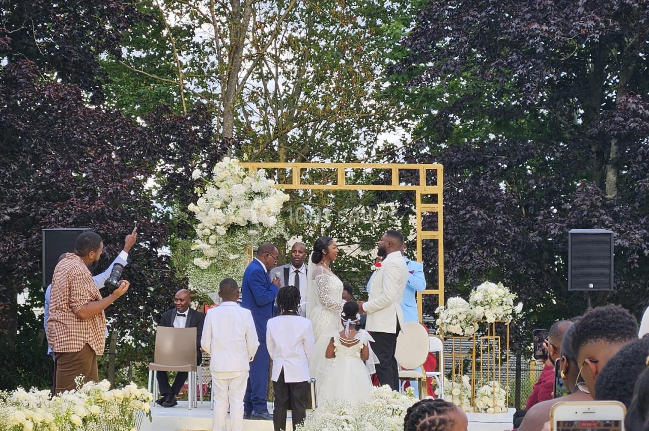 Cérémonie de mariage en extérieur avec des mariés devant une arche fleurie, entourés d'invités et d'enfants.